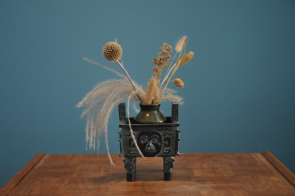 Bronze tripod with original dried flowers on teal wall