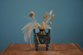 Bronze tripod with original dried flowers on teal wall